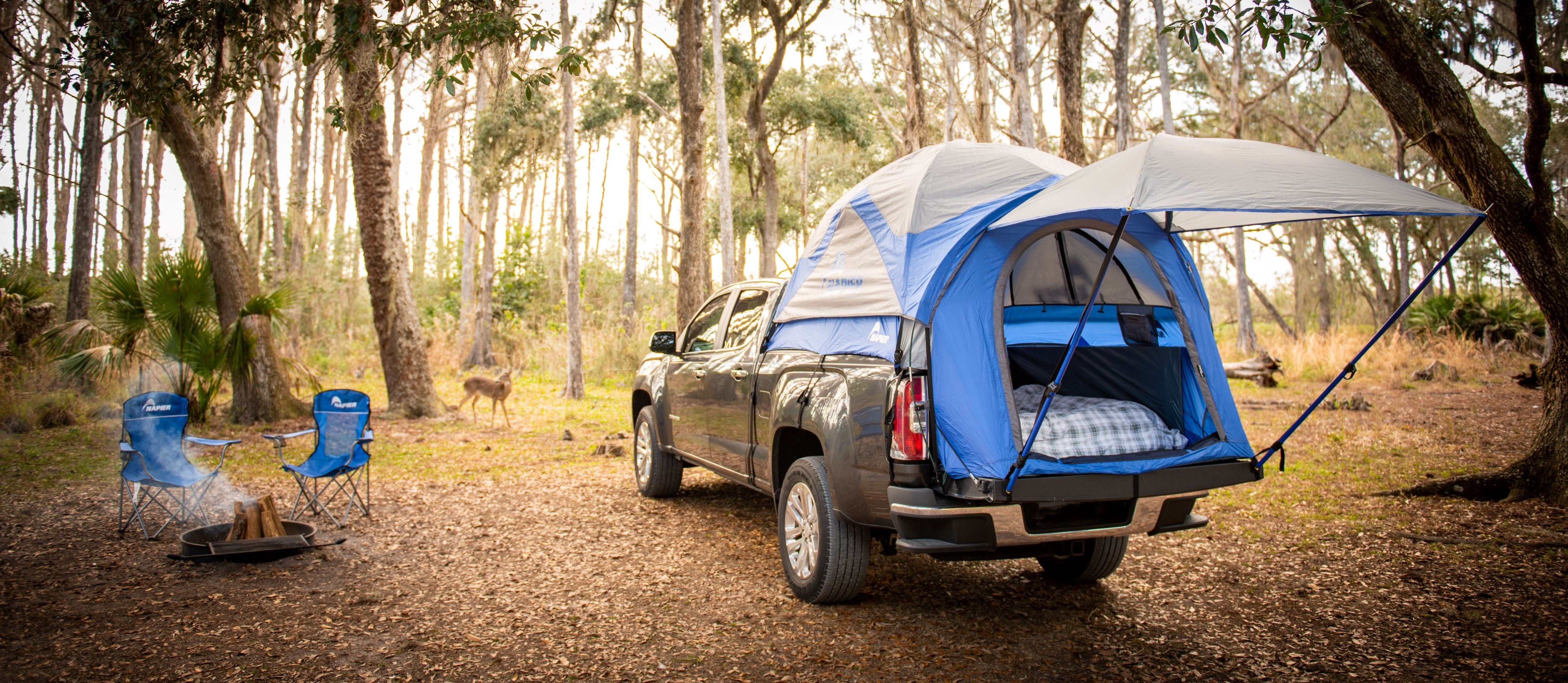 Napier truck tent camping set up with fire pit and two chairs in the forest