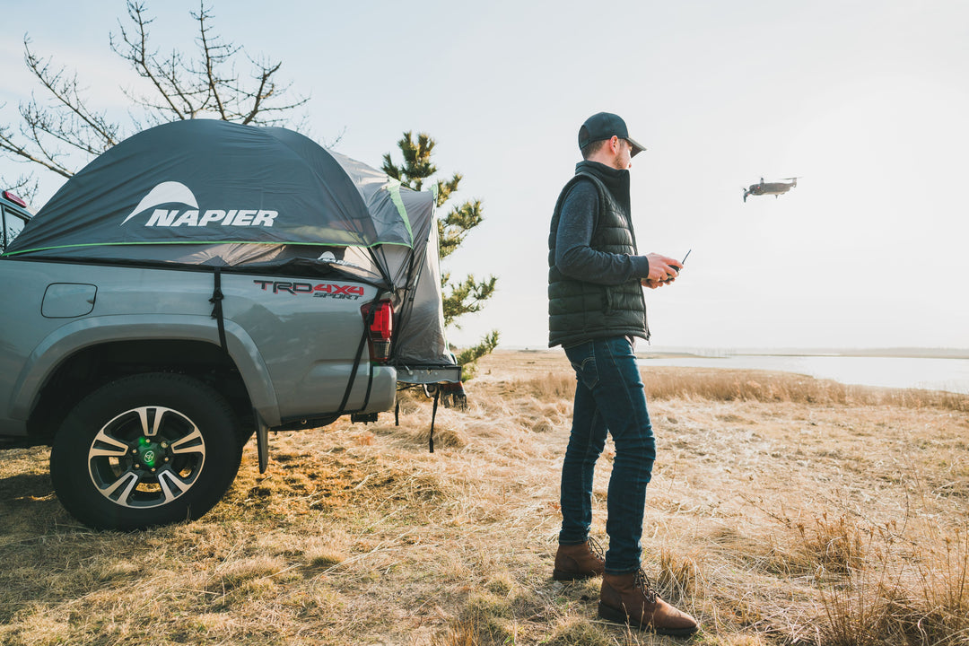 Person flying a drone next to their truck tent overlanding camping set up