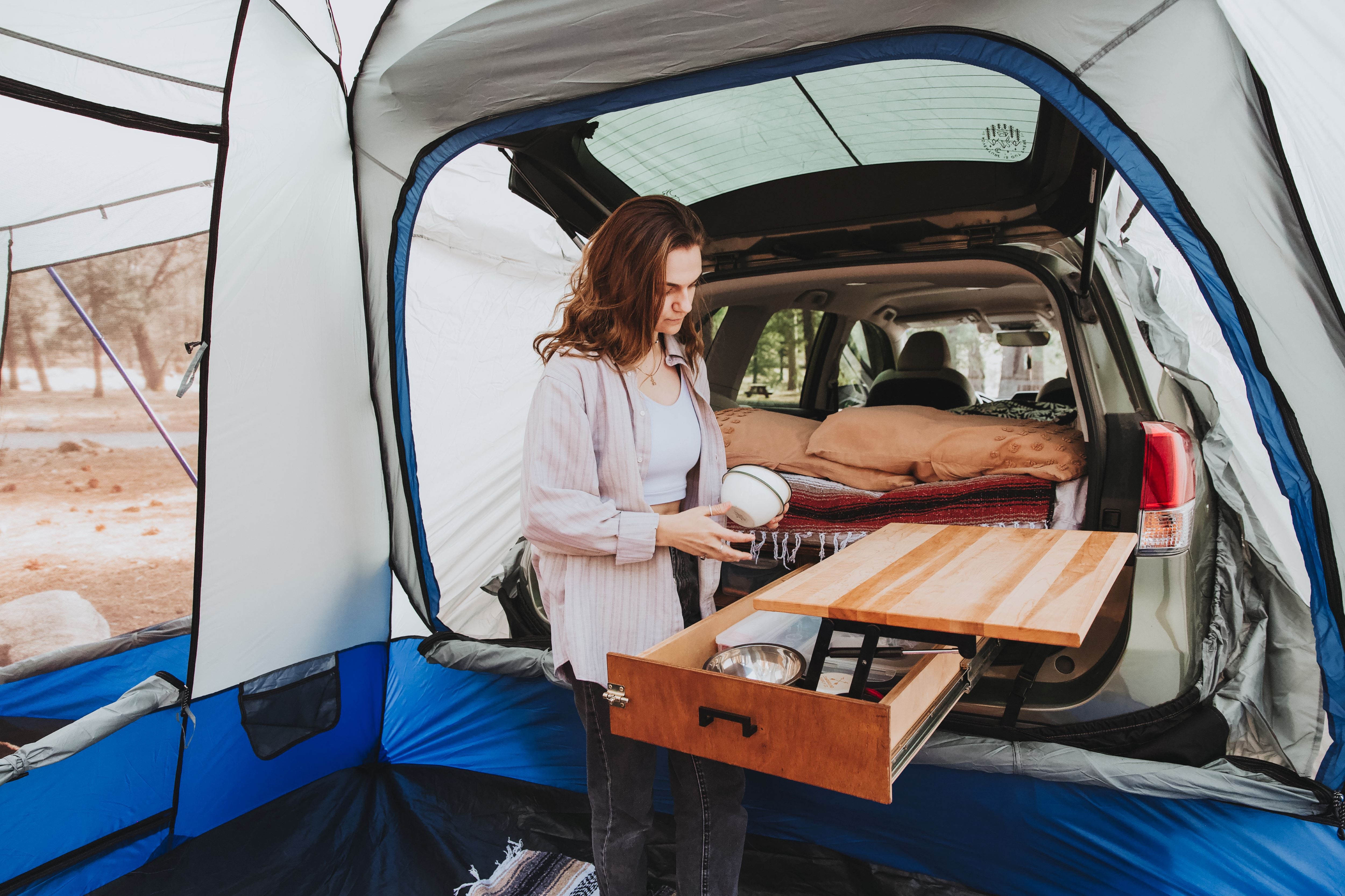 Girl inside an SUV tent camping set up with a pull out drawer and kitchen station