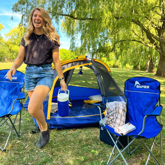 girl laughing and walking next to a ground tent and camping chairs