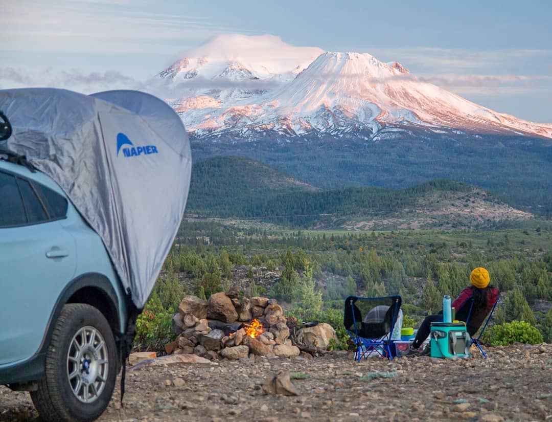 Person sitting at a camp fire with a napier sportz cove awning tent overlooking the mountains