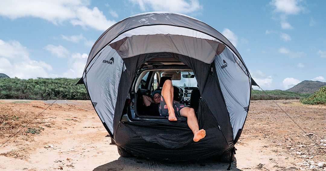 Man laying down inside a car with a napier sportz cove awning tent