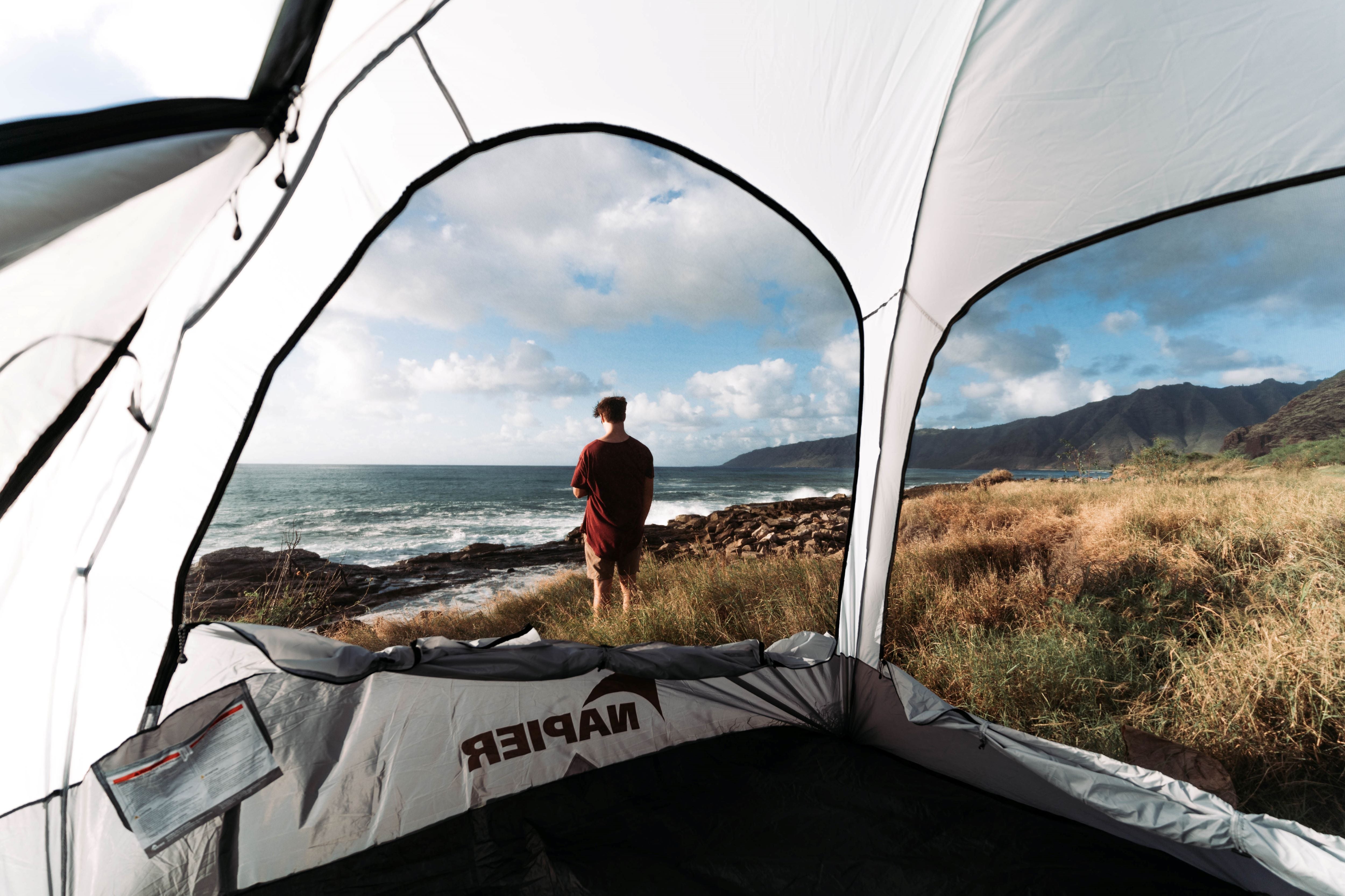 man standing outside suv tent next to the ocean