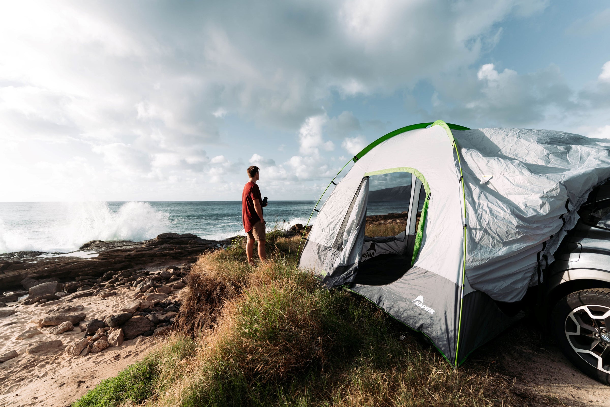 Man standing next to an suv tent camping set up next to the ocean