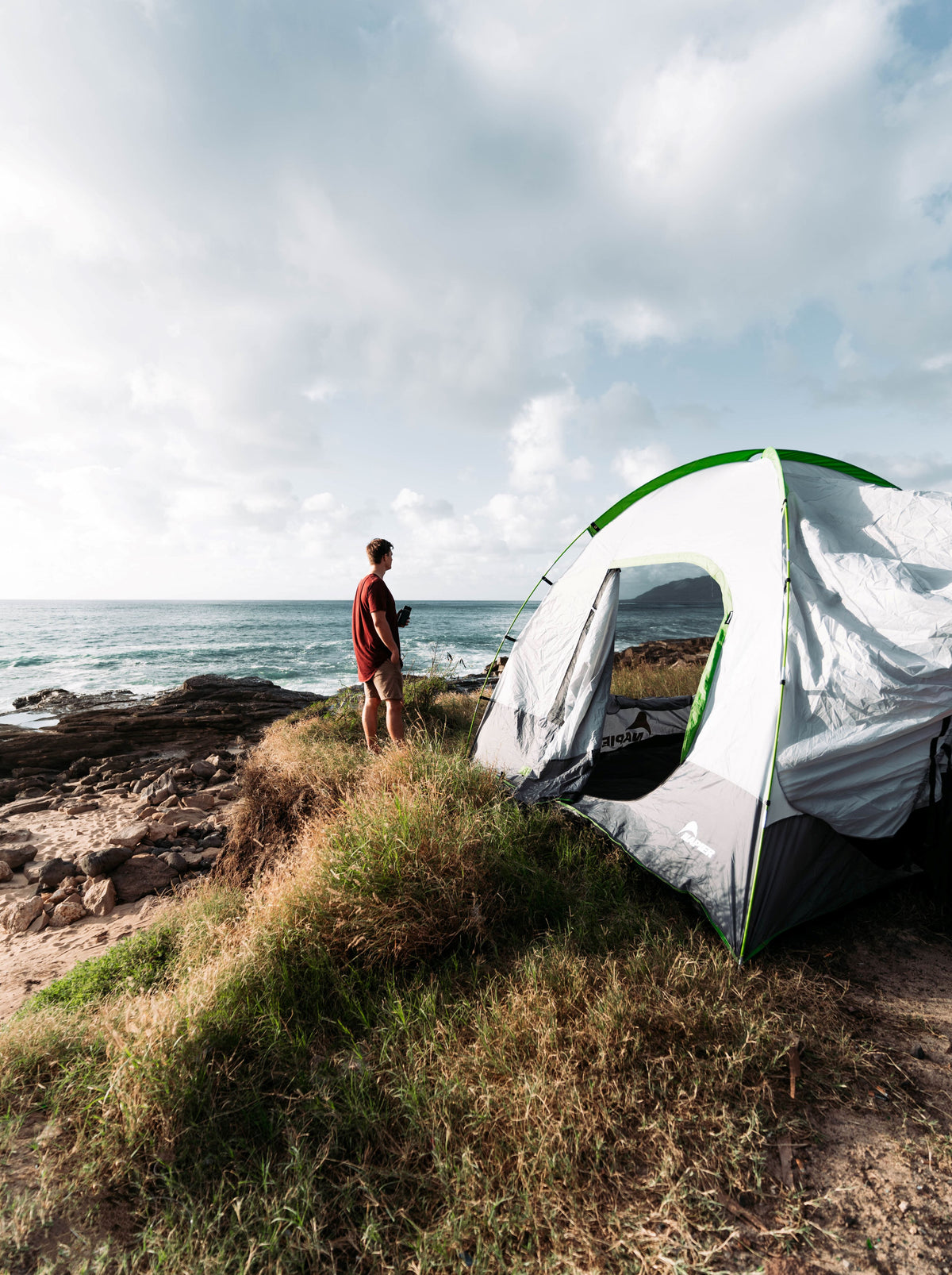 Man standing next to an suv tent camping set up next to the ocean