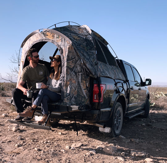 Couple sitting inside a camo truck tent set up