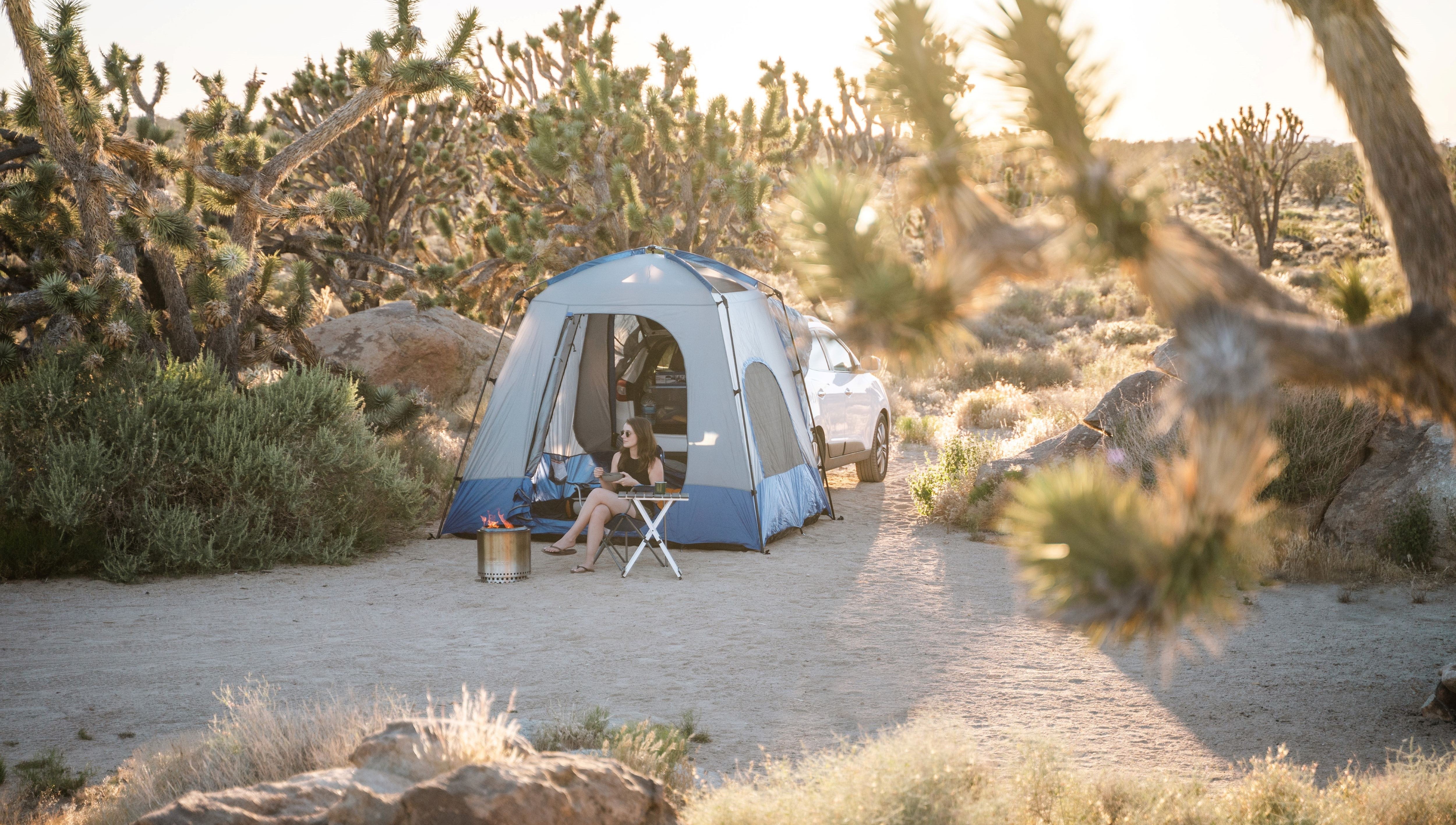 Girl sitting outside an suv tent camping set up in the desert