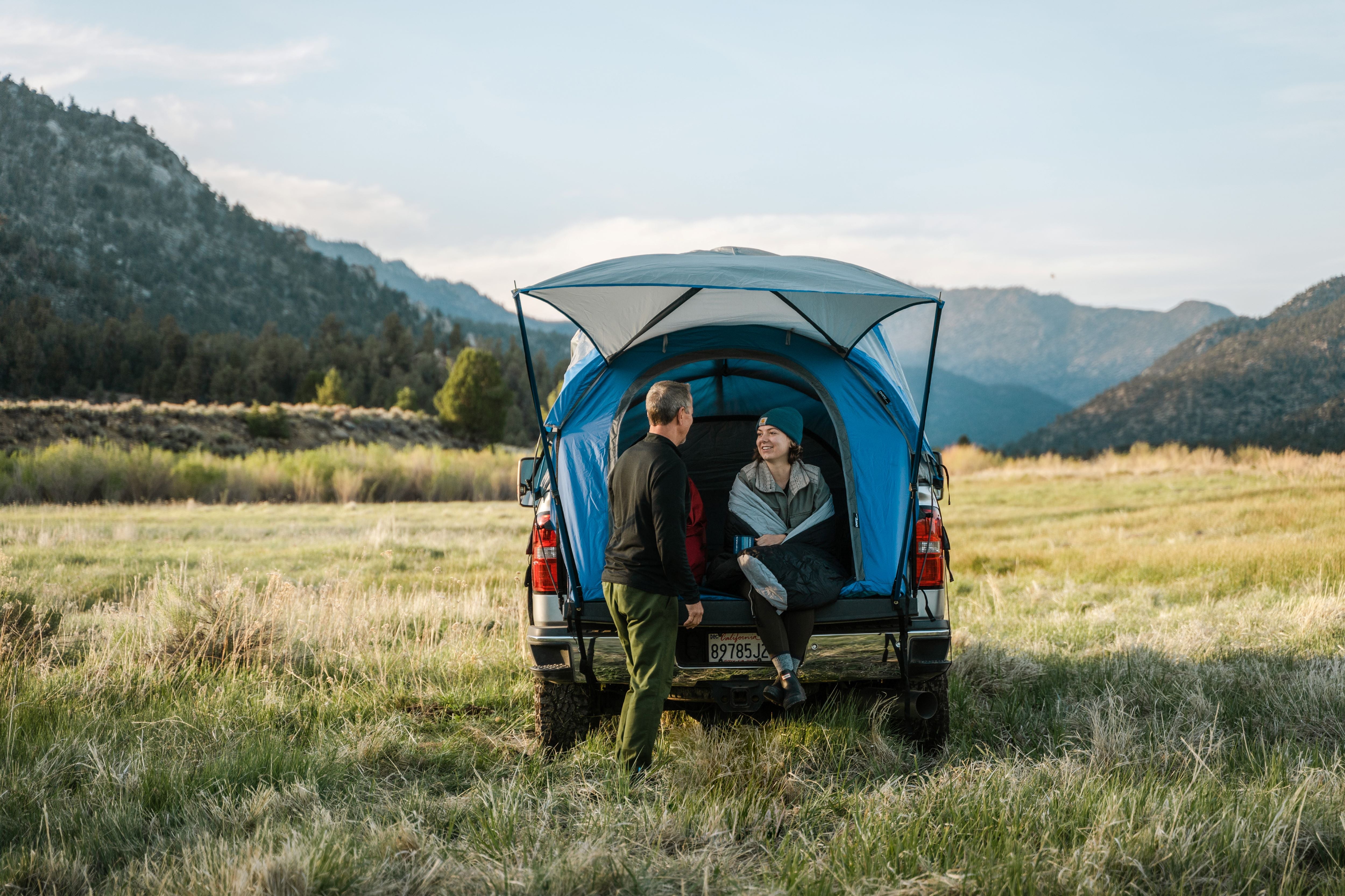 Two people sitting inside a napier truck tent camping set up in a field